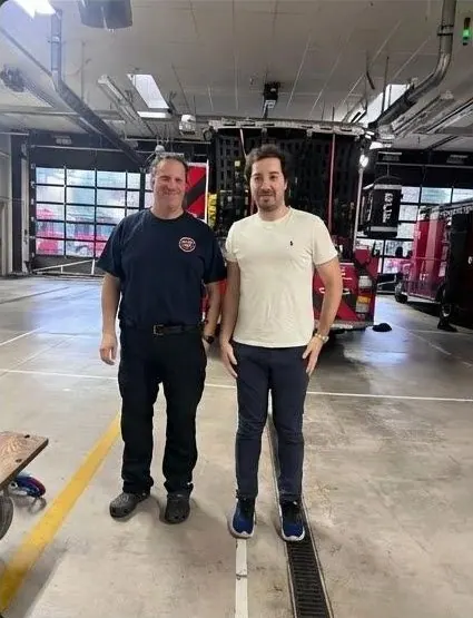 Furkan Serhatlıoğlu standing with a Seattle Fire Department firefighter inside a fire station, a fire engine behind them.